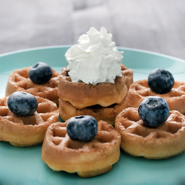 Las obleas con crema batida de arándanos se encuentran en un plato azul. Postre bellamente decorado.