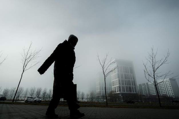 OBNINSK, Rusia - 2 de noviembre de 2021: silueta de una abuela sobre un fondo de árboles y casas en la niebla.