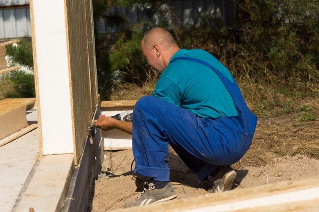 Obrero instalando paredes aisladas en un sitio de construcción arrodillado en el suelo para alinear la parte inferior del panel