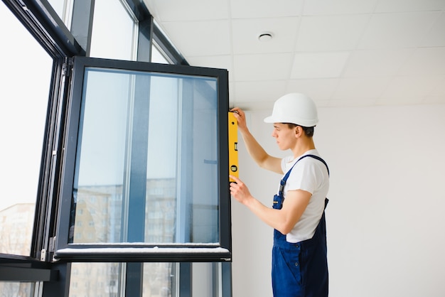 Obrero en monos instalando o ajustando ventanas de plástico en la sala de estar de casa