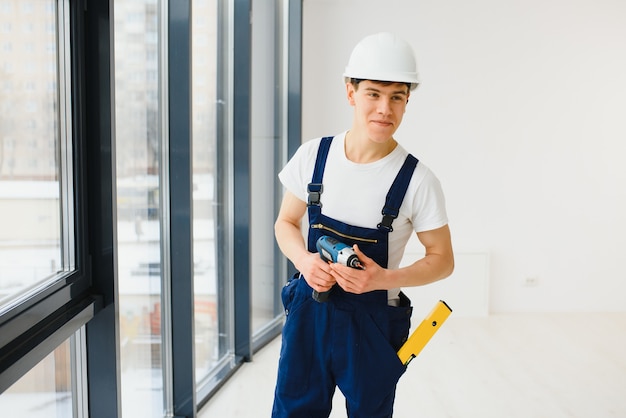 Obrero en monos instalando o ajustando ventanas de plástico en la sala de estar de casa