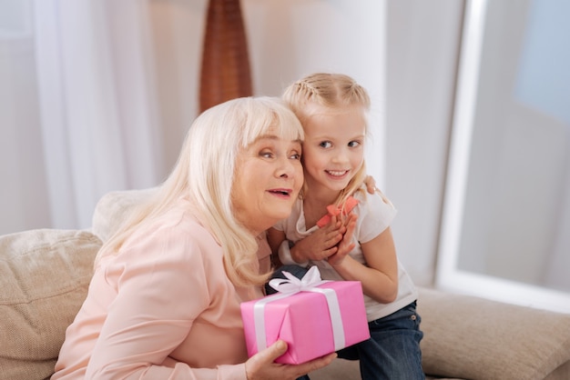 Foto obrigado por um presente. mulher idosa e simpática encantada sorrindo e segurando uma caixa de presente enquanto abraça a neta