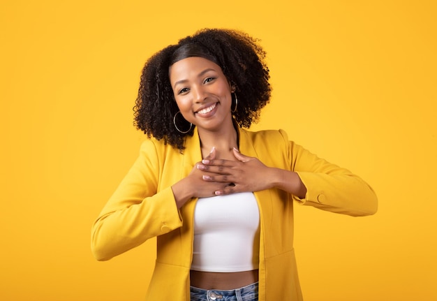 Obrigado senhora negra agradecida pressionando as mãos no peito e sorrindo em pé posando sobre o estúdio amarelo