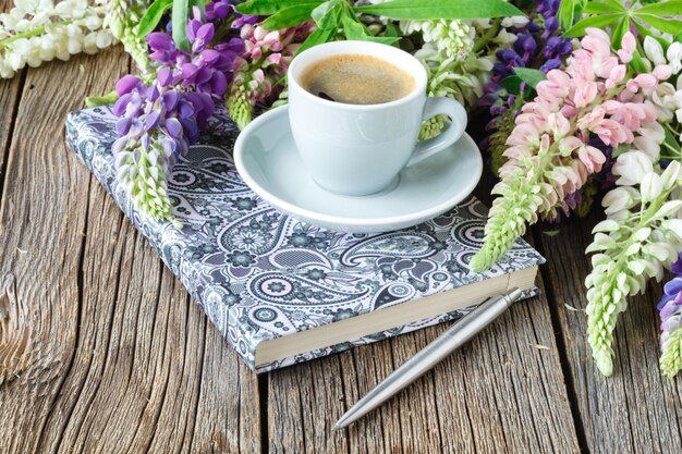 Observe com uma caneta e uma xícara de café, tremoços flores na mesa de madeira