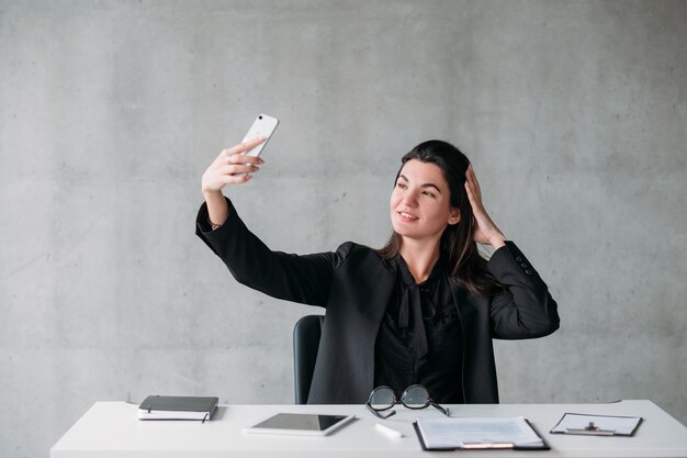 Obsessão pelas redes sociais. Mulher de negócios narcistas tomando selfie em sua mesa de escritório, posando.