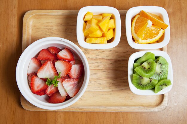 Obst in der Mini-Tasse auf dem Holztablett, Erdbeere, Mango, Kiwi und Orange