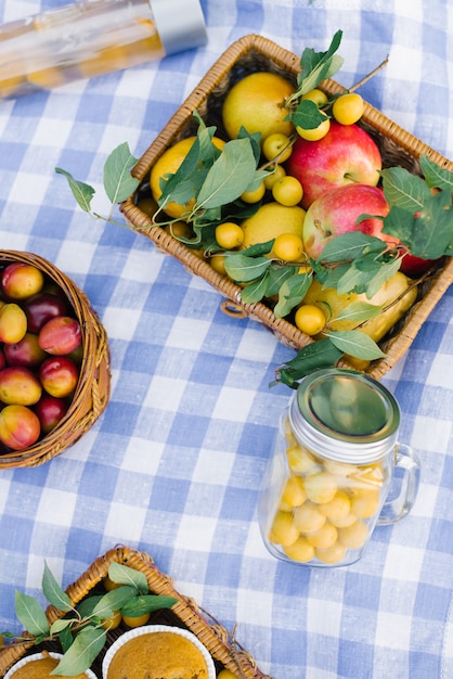 Obst und Beeren in Picknickkörben auf einer blau-weiß karierten Tischdecke auf einem grünen Rasen und frischem Gebäck