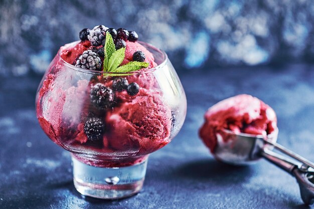 Obst- und beereneis in einem großen schönen glas, verziert mit blättern von minze und schaufel auf schwarzem stein, kopie, textraum