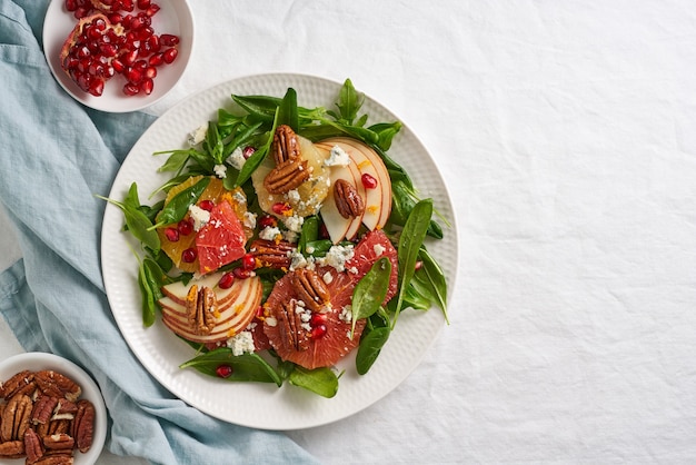 Obst-Zitronensalat mit Nüssen, grünen Salatblättern. Ausgewogenes Essen. Spinat mit Orange, Grapefruit, Äpfeln, Pekannüssen und Gorgonzola, garniert mit Granatapfelkernen, Draufsicht, Kopierraum