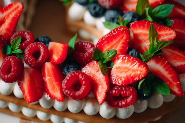 Obstkuchen. Backen Sie verziert mit Beeren auf einem hölzernen Stand auf einem Schwarzen zusammen.