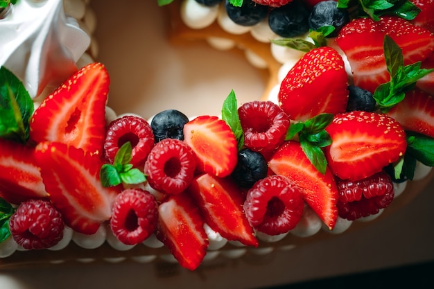 Obstkuchen. Backen Sie verziert mit Beeren auf einem hölzernen Stand auf einem Schwarzen zusammen.