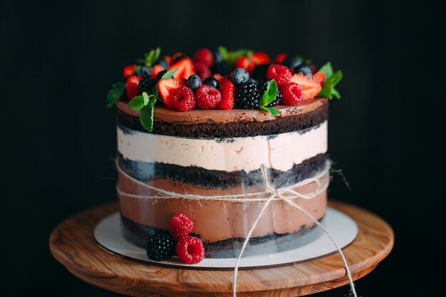 Obstkuchen. Backen Sie verziert mit Beeren auf hölzernem Stand auf Schwarzem zusammen