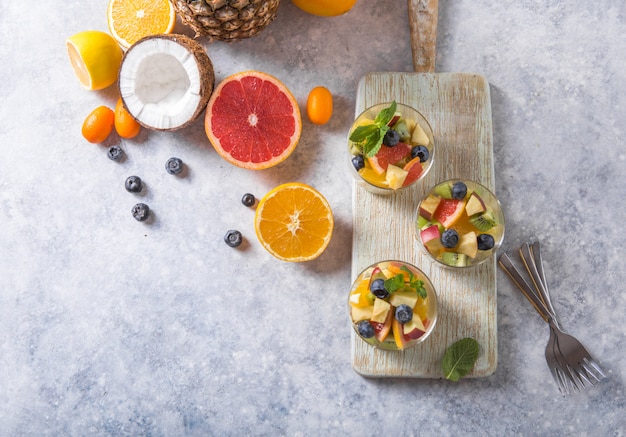 Obstsalat in den Gläsern, frische Sommernahrungsmittel, gesunde organische orange Kiwiblaubeerananaskokosnuss. Ansicht von oben