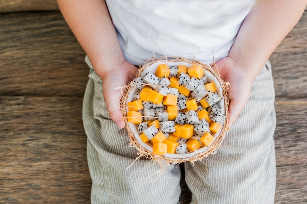 Obstsalat mit Drachenfrucht und Papaya in einer halben Kokosnuss in der Hand