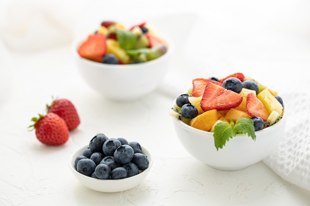 Obstsalat mit Erdbeeren, Kiwi-Aprikosen und Blaubeeren in weißen Tellern auf einem weißen Tisch