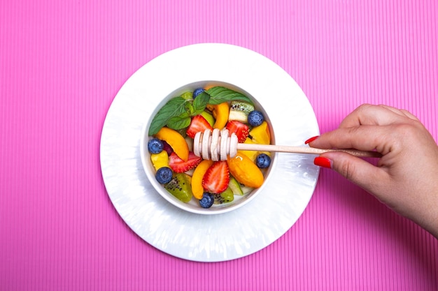 Obstsalat mit hölzernem Honiglöffel auf rosa Hintergrund