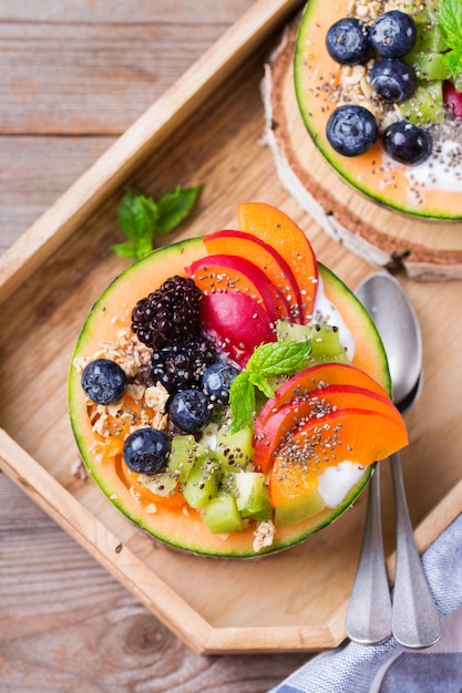 Obstsalat mit Joghurt in geschnitzter Melone Cantaloupe Schüssel auf Tisch