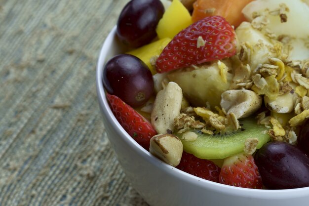 Obstsalat mit Kastanien und Müsli in einer Schüssel reife Früchte Ananas Mango Traube Erdbeere Papaya