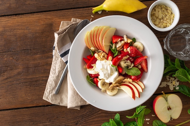 Obstsalatschüssel auf einer Draufsicht des Holztischs. Gesundes Sommeressen