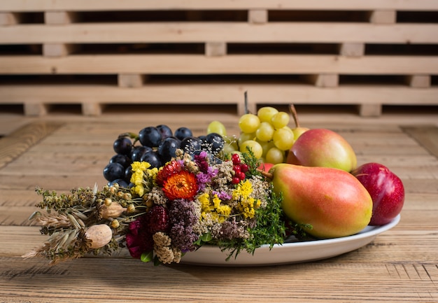 Obstteller mit Dekorationen der wilden Blume auf der hölzernen Tabelle