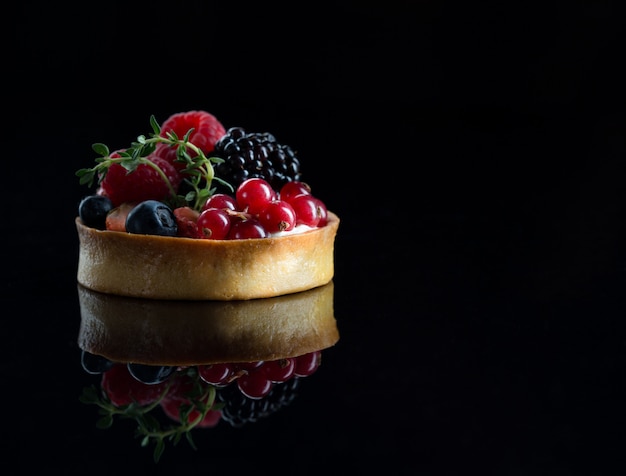 Obsttörtchen mit frischen Himbeeren, Blaubeeren und Ment an der schwarzen Wand