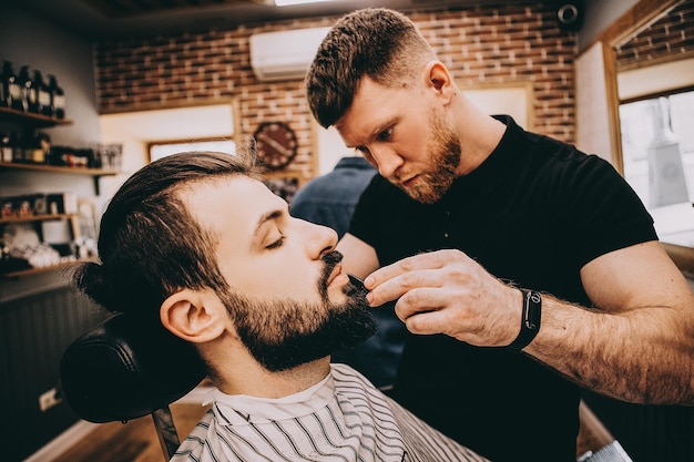 Obtendo a forma perfeita Vista lateral de um jovem barbudo estiloso cortando o cabelo da barba