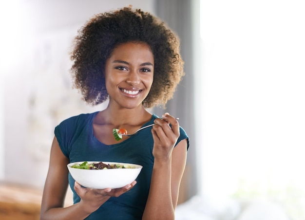 Foto obtendo seus verdes retrato de uma jovem atraente comendo uma tigela de salada