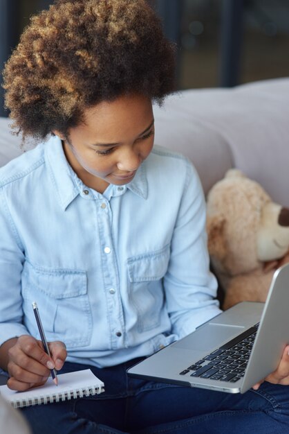 Obtenga nuevos conocimientos centrados en la colegiala adolescente usando la computadora portátil tomando notas durante la lección en línea mientras