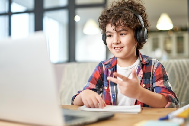 Obtenha mais conhecimento menino latino-americano feliz usando fones de ouvido olhando para a tela de