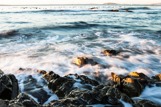 Océano rocoso y agua con olas en la playa para el paisaje ambiental y el cielo azul Verano tranquilo y natural con paisaje marino matutino en el horizonte para la costa tropical marina y la naturaleza de larga exposición