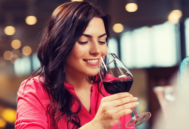 Foto ocio, bebidas, degustación, gente y vacaciones concepto - mujer sonriente bebiendo vino rojo en un restaurante