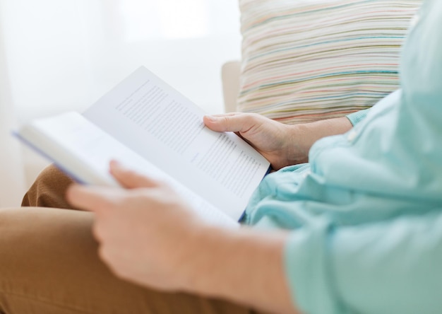 ocio, educación, literatura y concepto de hogar - cerca del hombre y sentado o acostado en el sofá y leyendo un libro en casa