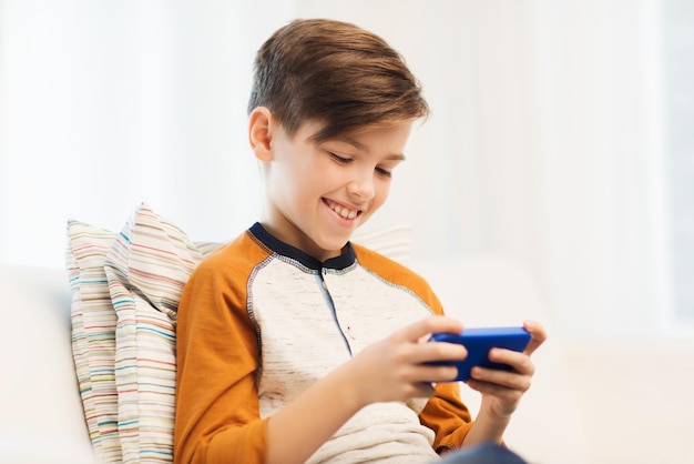 ocio, niños, tecnología, comunicación por Internet y concepto de personas - niño sonriente con mensaje de texto de smartphone o jugando en casa