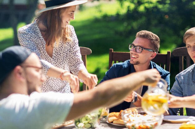 ocio, vacaciones, comida, gente y concepto de comida - amigos felices cenando y compartiendo ensalada en la fiesta del jardín de verano