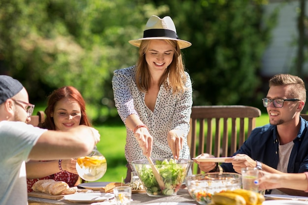 ocio, vacaciones, comida, gente y concepto de comida - amigos felices cenando y compartiendo ensalada en la fiesta del jardín de verano