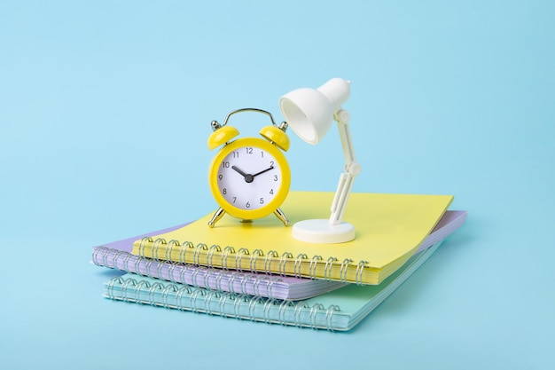 Foto oclock amarelo brilhante e lâmpada branca ficando em cima de notebooks em cores pastel