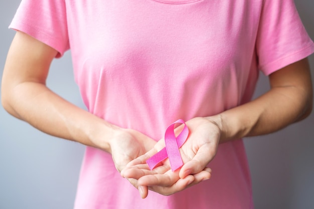 Octubre mes de concientización sobre el cáncer de mama, anciana en camiseta rosa con una mano sujetando la cinta rosada para apoyar a las personas que viven y padecen enfermedades. Concepto del día internacional de la mujer, la madre y el cáncer mundial