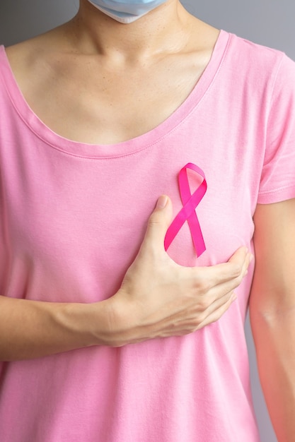 Octubre mes de concientización sobre el cáncer de mama, anciana en camiseta rosa con una mano sujetando la cinta rosada para apoyar a las personas que viven y padecen enfermedades. Concepto del día internacional de la mujer, la madre y el cáncer mundial