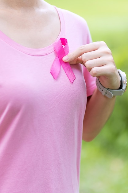 Octubre mes de concientización sobre el cáncer de mama, mujer adulta con camiseta rosa con una mano sujetando la cinta rosada para apoyar a las personas que viven y padecen enfermedades. Concepto del día internacional de la mujer, la madre y el cáncer mundial