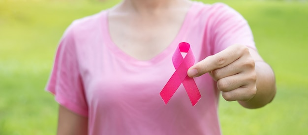 Octubre mes de concientización sobre el cáncer de mama, mujer adulta con camiseta rosa con una mano sujetando la cinta rosada para apoyar a las personas que viven y padecen enfermedades. Concepto del día internacional de la mujer, la madre y el cáncer mundial