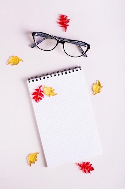 Óculos de bloco de notas vazios de vida de outono e folhas coloridas em um fundo rosa top e vertical