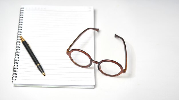 Óculos de caderno mínimos e caneta em mesa branca