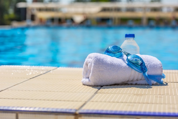 Óculos de natação uma toalha branca e uma garrafa de água na beira da piscina