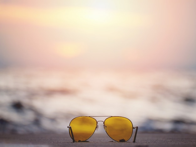 Óculos de sol com lente amarela na areia na praia do sol.