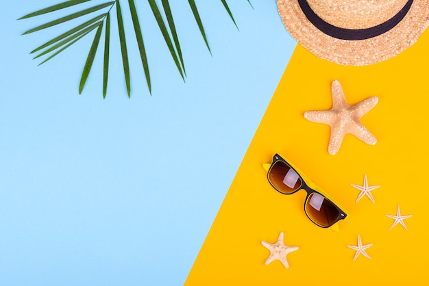 óculos de sol e chapéu com conchas e estrelas do mar em uma superfície colorida