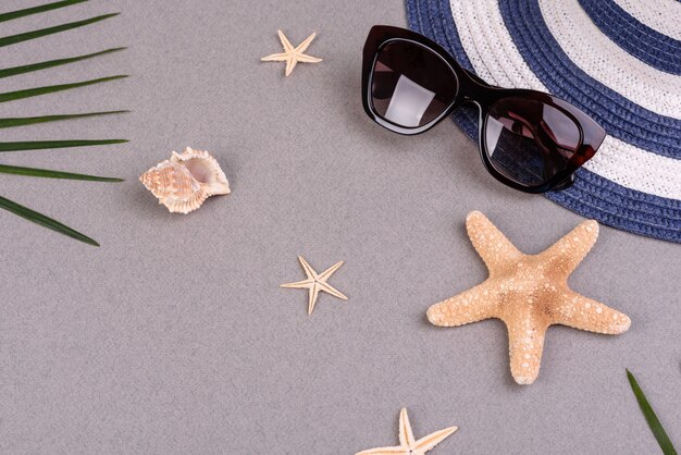 óculos de sol e chapéu com conchas e estrelas do mar em uma superfície colorida