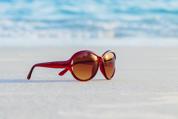 Óculos de sol marrons na areia linda praia de verão