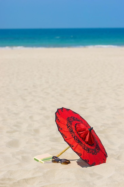 Óculos de sol tradicionais birmaneses e um livro estão espalhados na areia branca à beira-mar