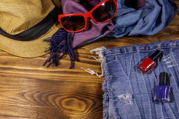 Óculos de sol vermelhos chapéu de palha cachecol de verão shorts jeans e esmalte em fundo de madeira acessórios de moda feminina férias de verão e conceito de viagem