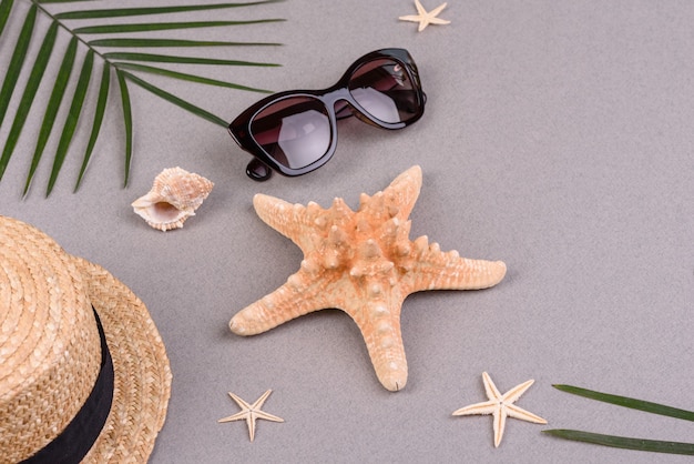 óculos e chapéu com conchas e estrelas do mar em uma superfície colorida